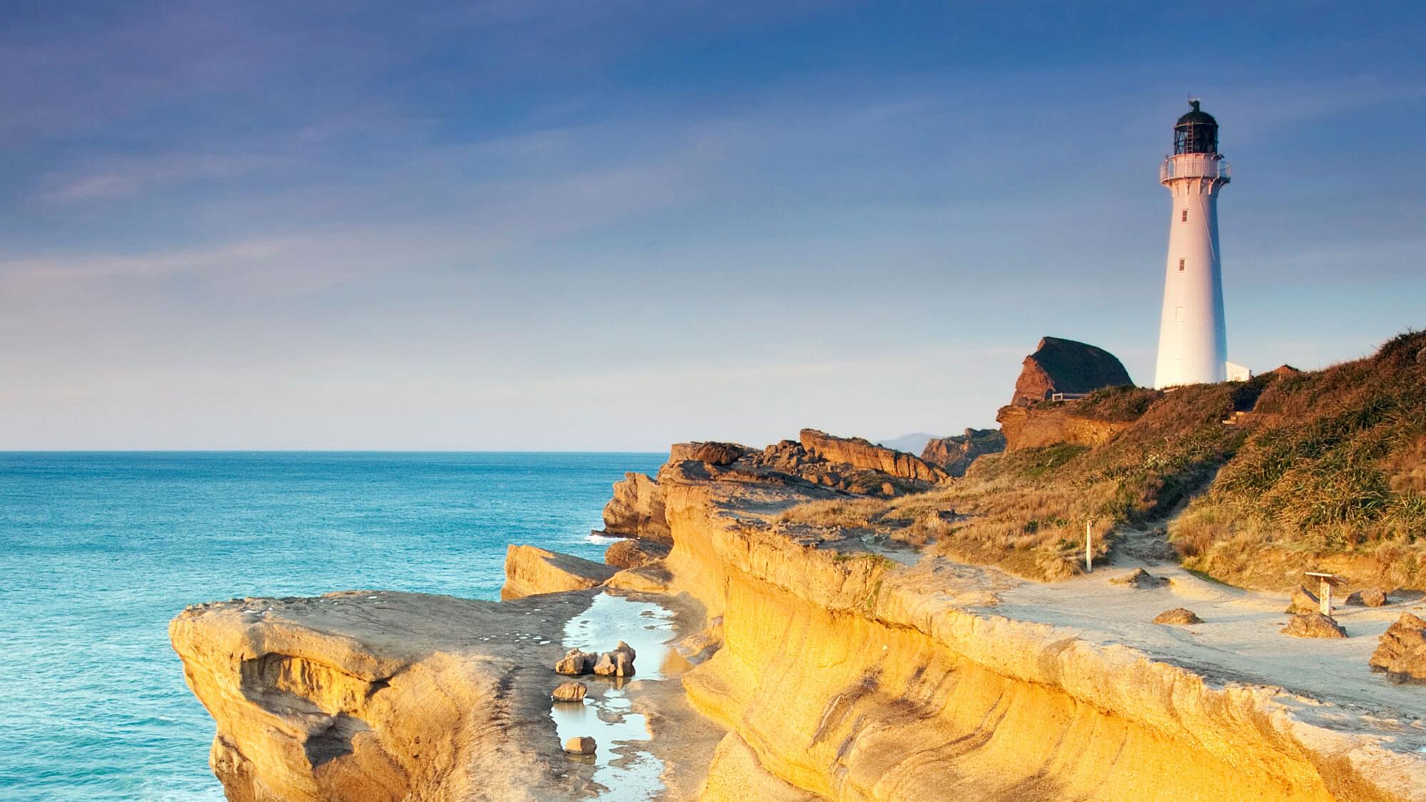 A lighthouse at the top of a cliff, overlooking the sea.