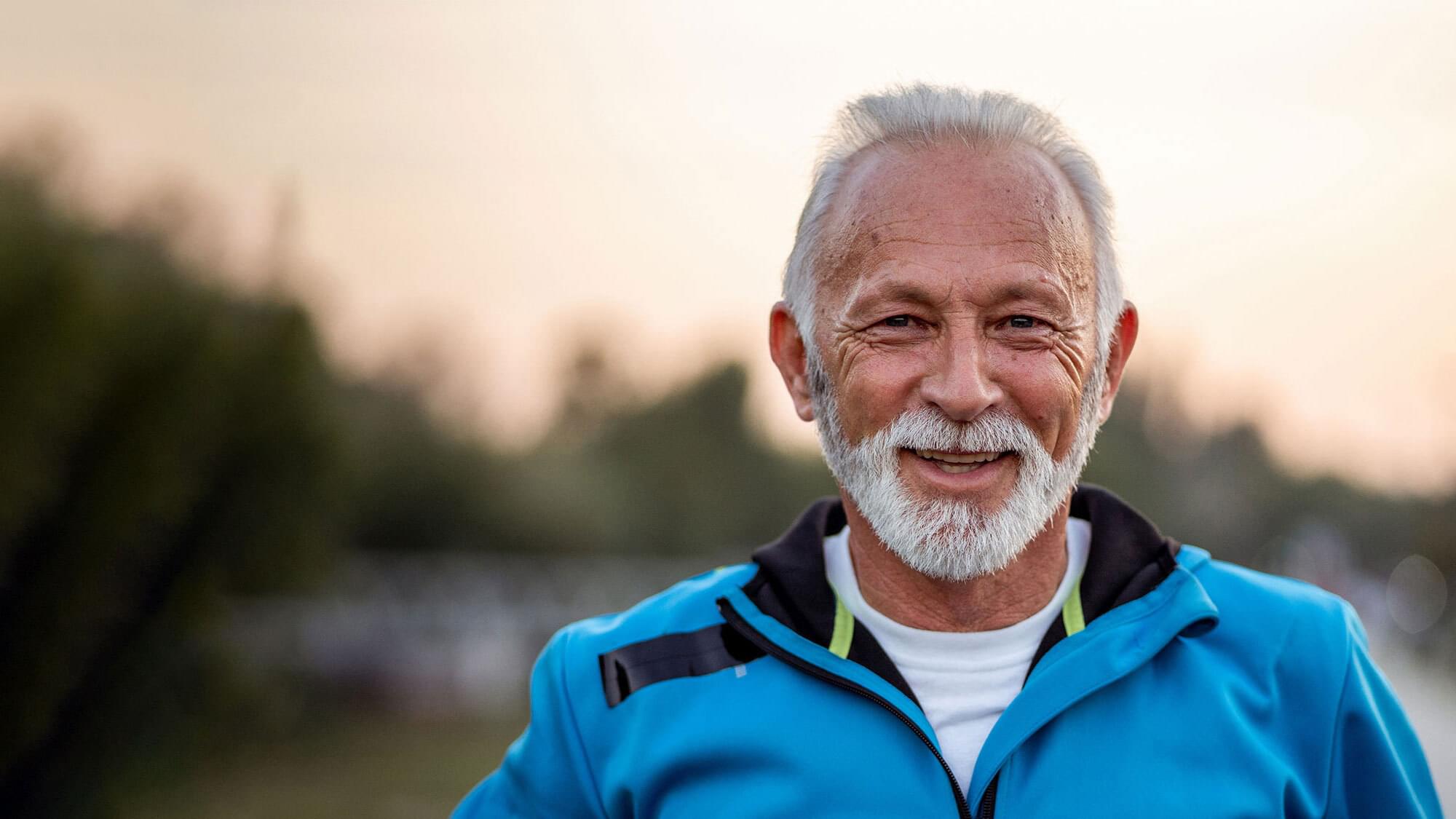 Active senior man is looking at the camera and smiling on the running track outdoors.